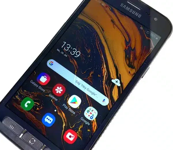 A person holding the Samsung Galaxy Xcover 4s in one hand while hiking through rugged terrain.